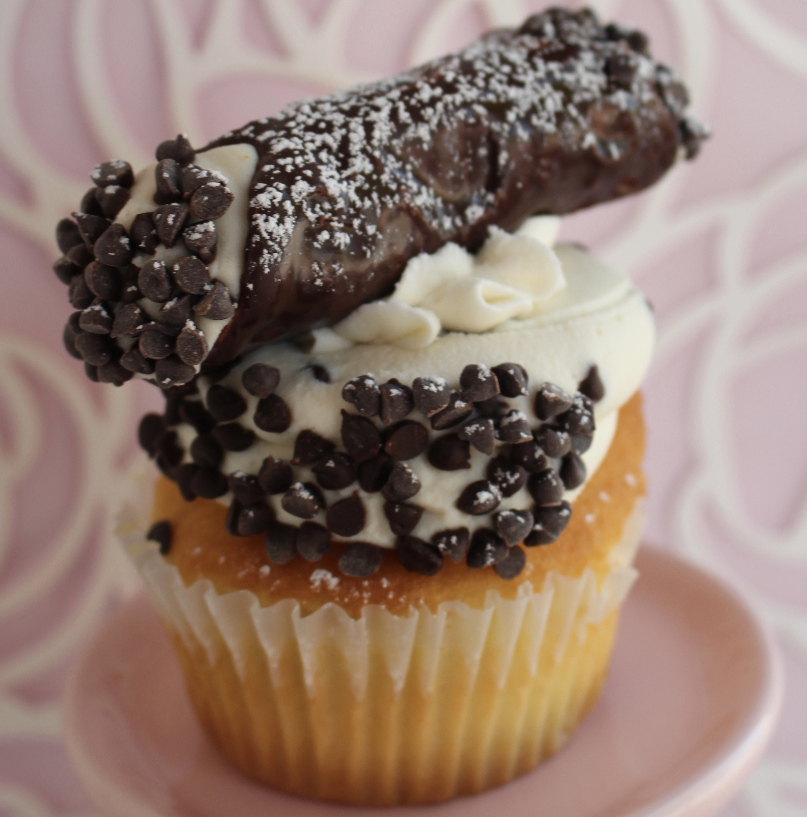 Vanilla cake with a cannoli cream, chocolate chips, and a whole mini cannoli on top!